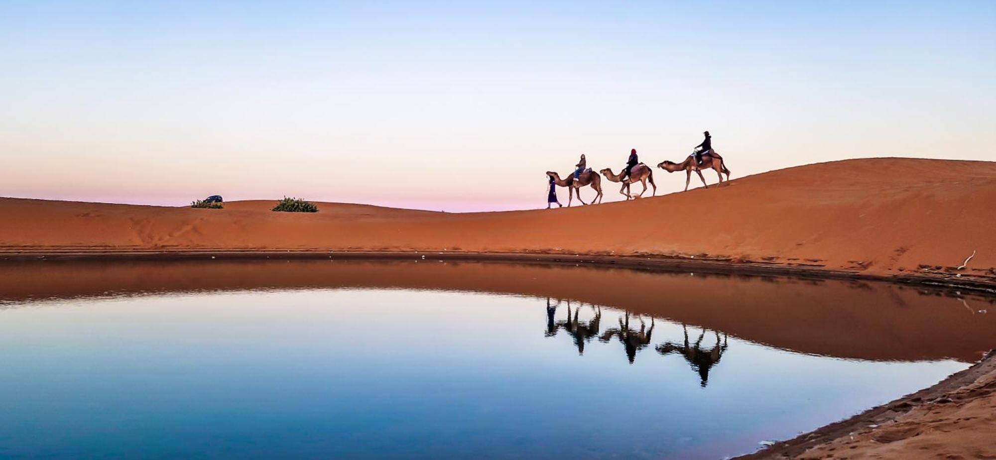 Caravane reflétée dans l’eau au pied des dunes